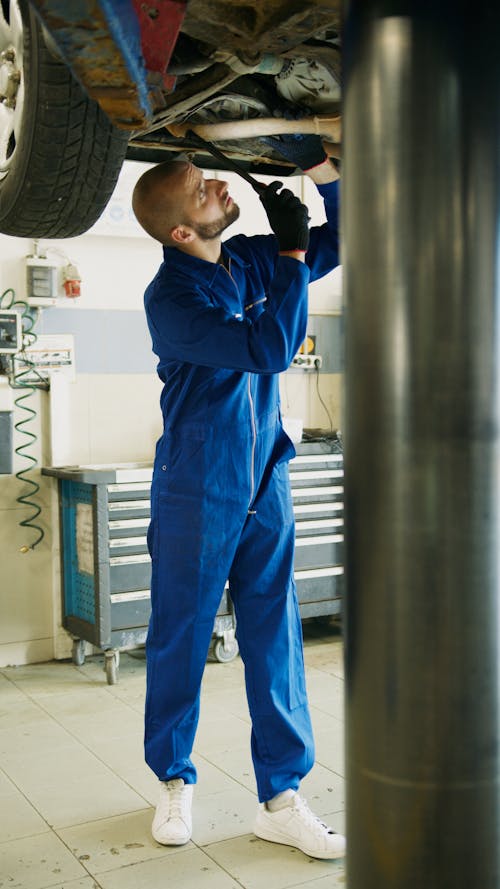 A Man in Blue Coverall Repairing a Vehicle