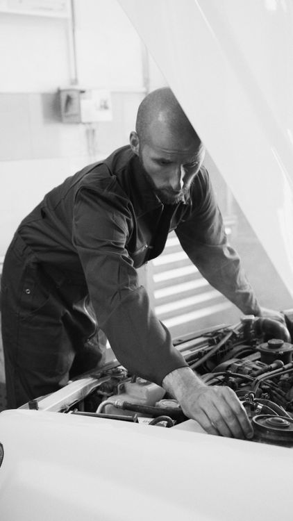Mechanic working under a car hood in a workshop