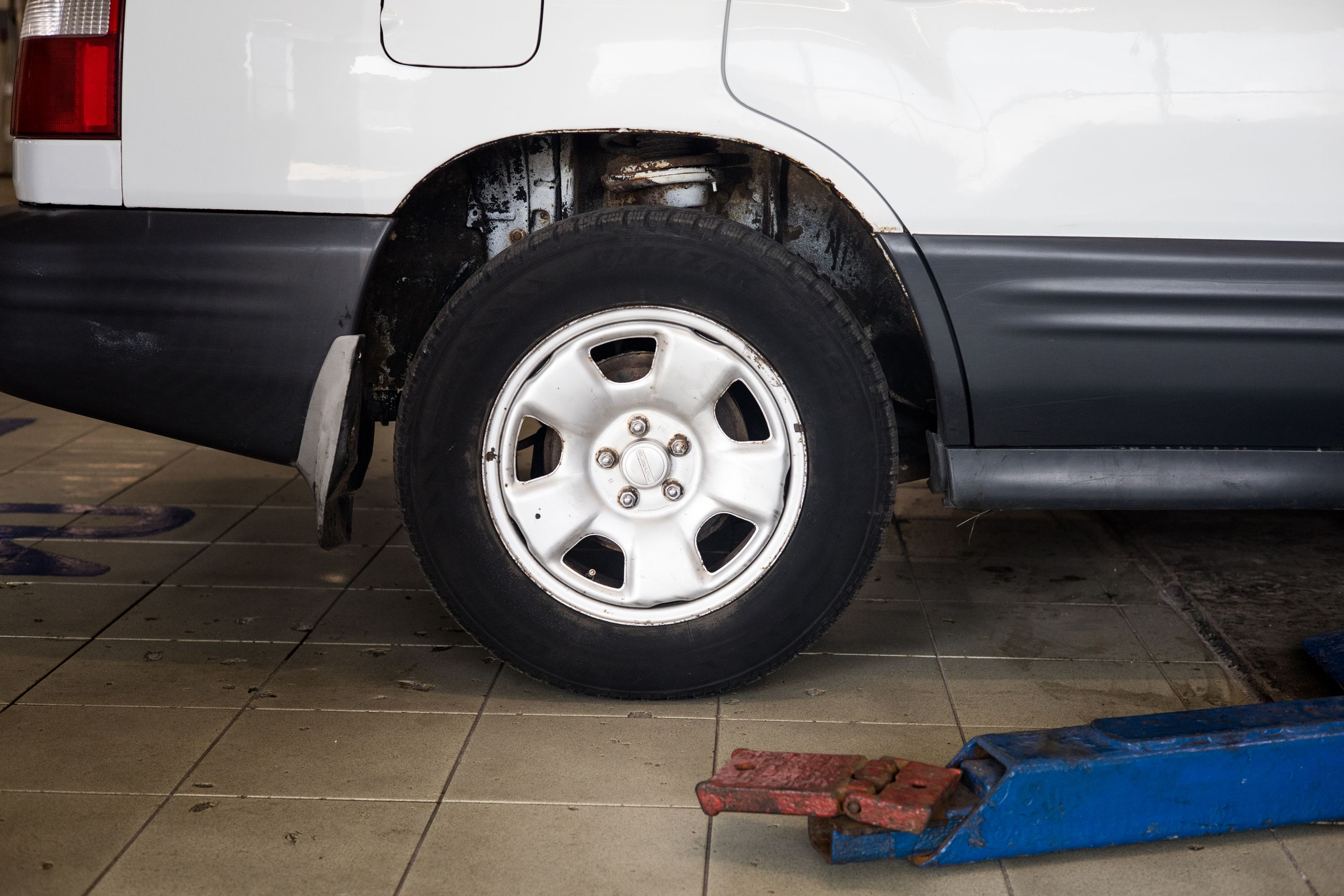 Hydraulic floor jack positioned under a vehicle's rear wheel before lifting for tire and brake work