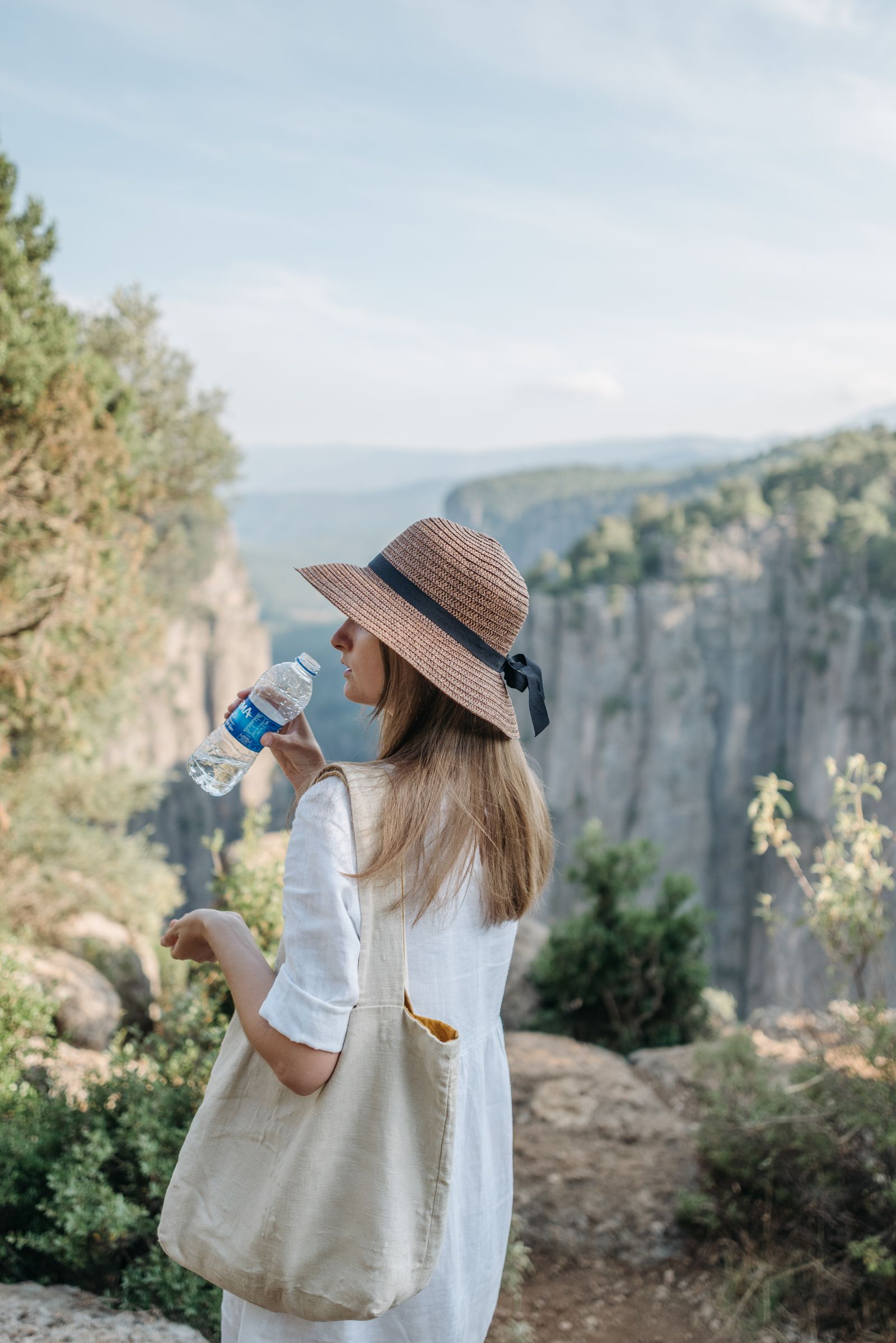 A woman in a sun hat looking across a deep green canyon