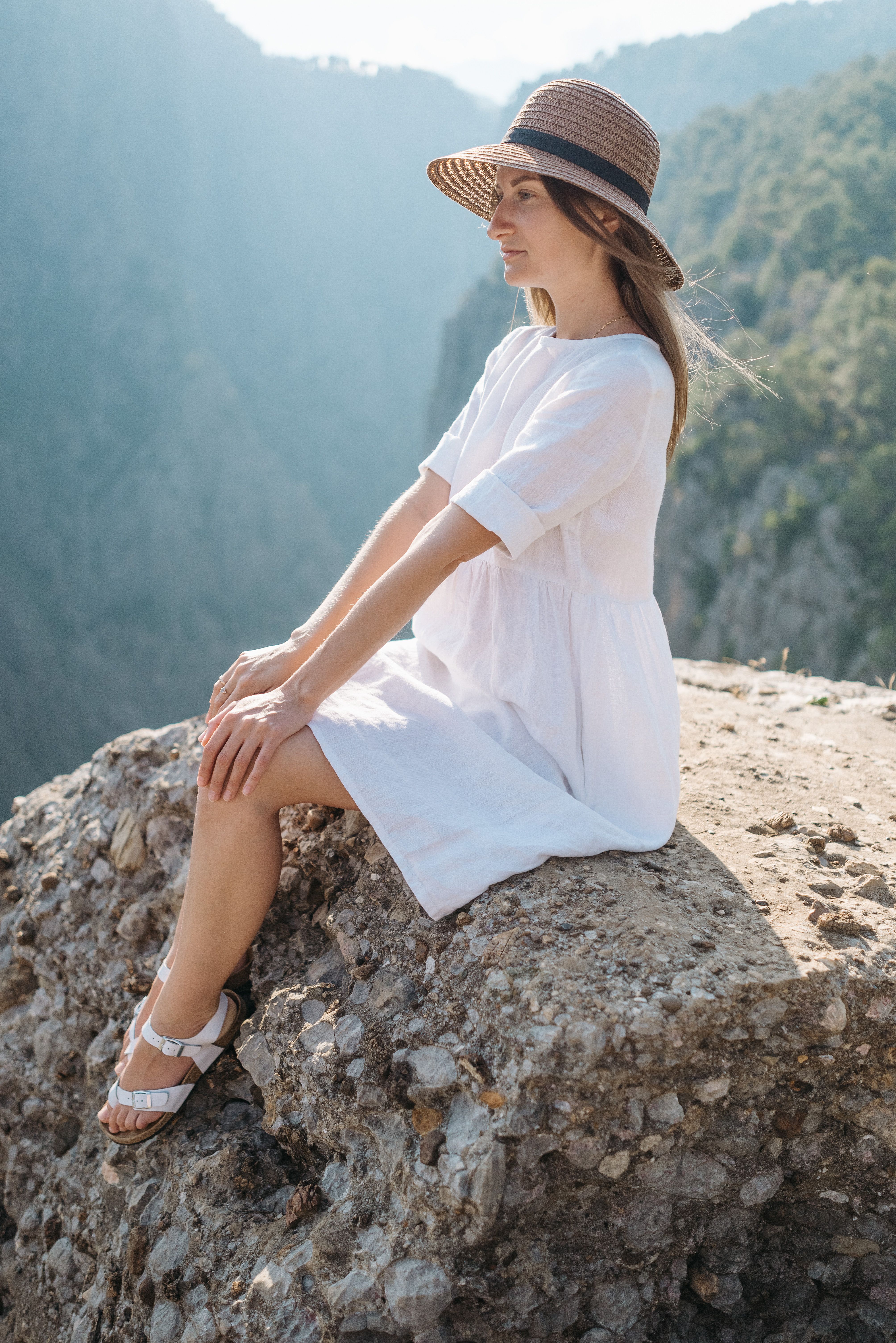 Woman in White Dress Wearing Hat Sitting on Cliff · Free Stock Photo