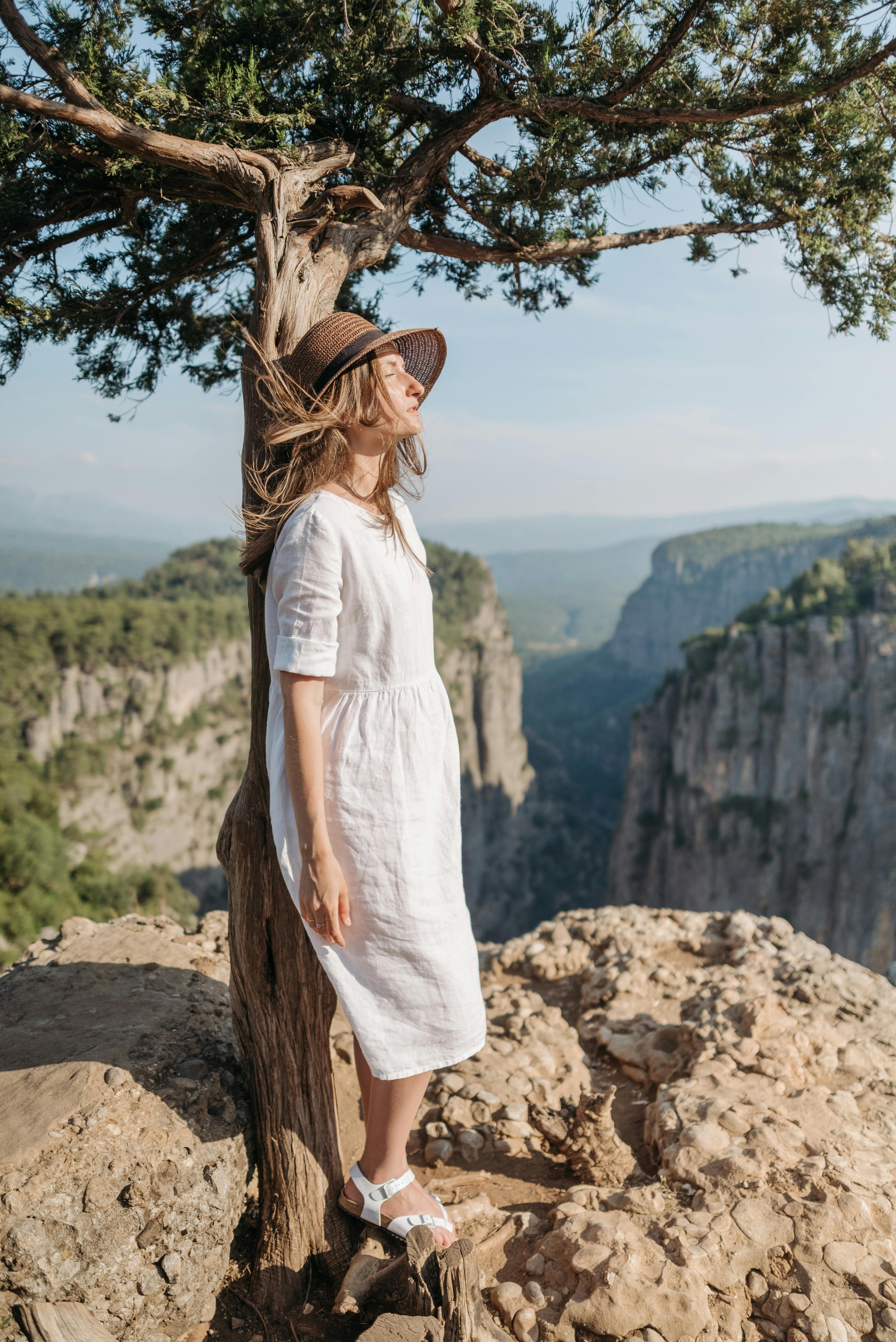 woman in white dress wearing hat leaning against tree