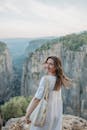 一个穿着白色连衣裙的微笑的女人站在悬崖边，欣赏风景