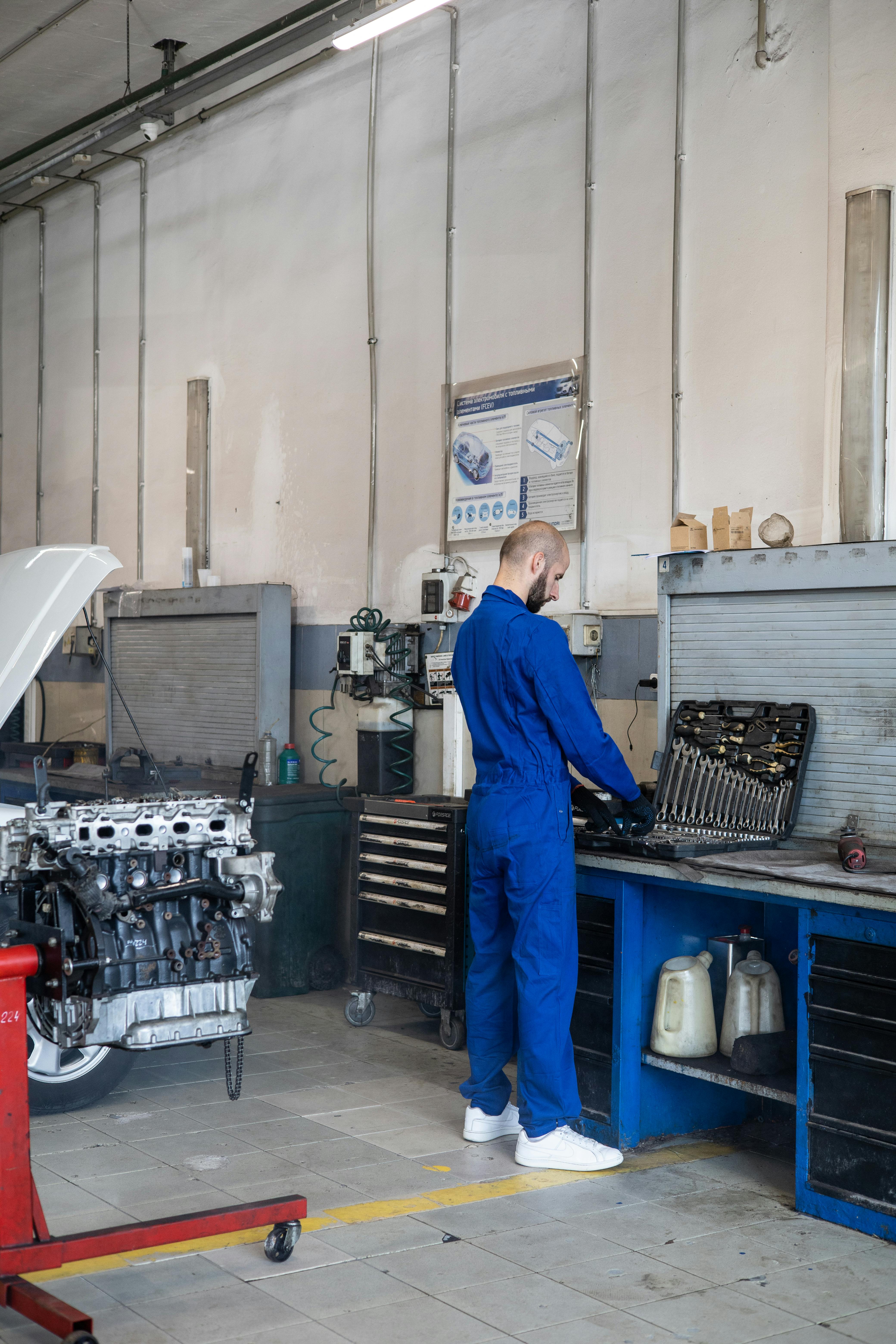 Auto mechanic in blue jumpsuit working on car parts in a garage workshop.