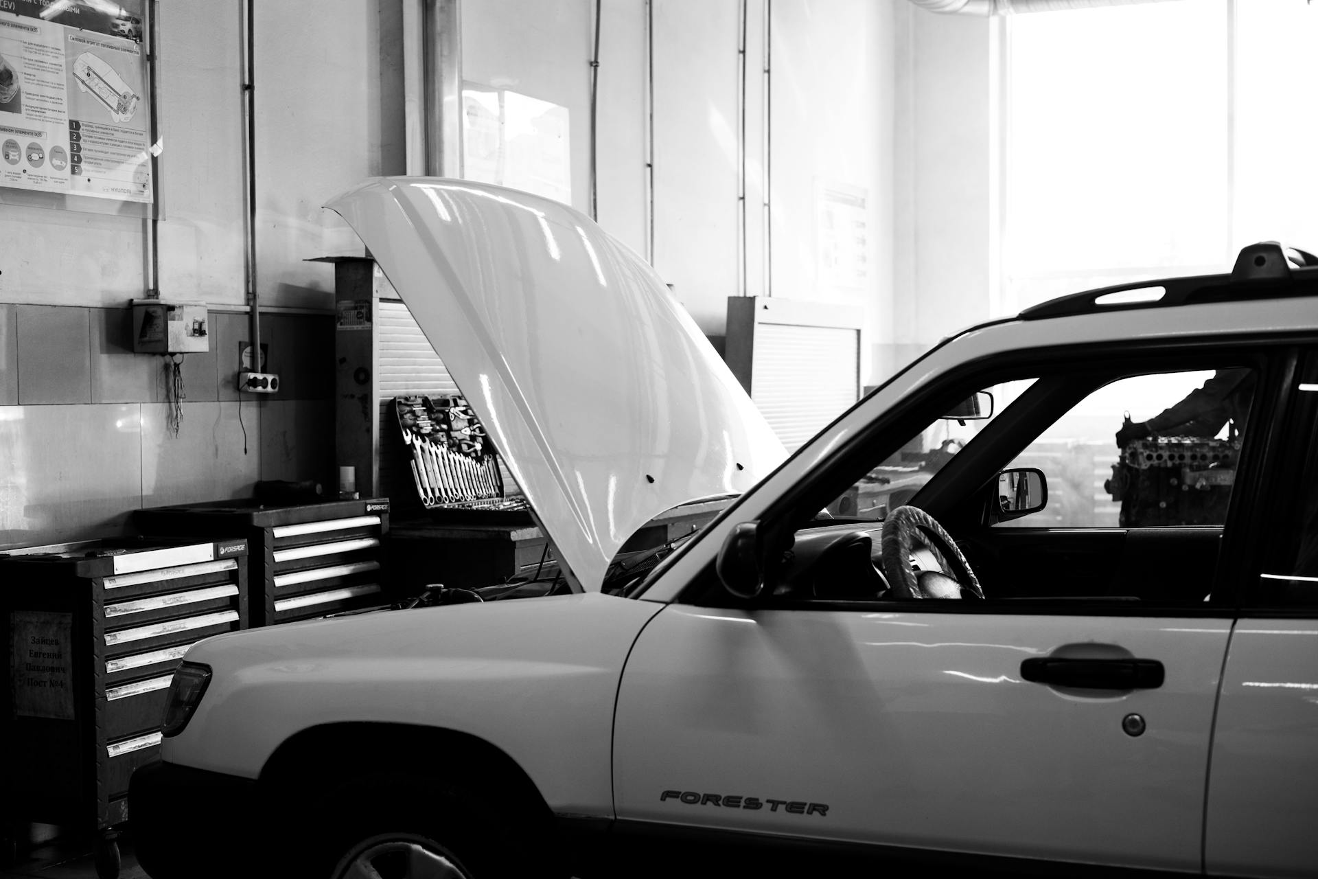 Black and white photo of a car in an auto repair shop. Hood open for maintenance.