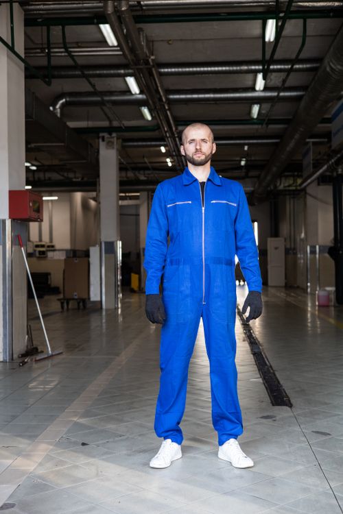 Free Mechanic in blue coverall standing confidently in an auto repair shop. Stock Photo