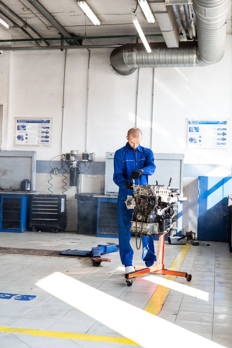 Mechanic in blue coveralls fixing an engine in a brightly lit auto repair shop.