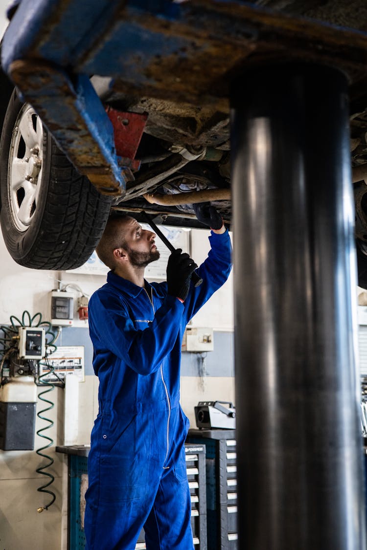 A Mechanic In Blue Coverall Working Under A Vehicle