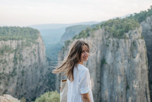 A woman in a white dress smiles as she overlooks a scenic canyon landscape.