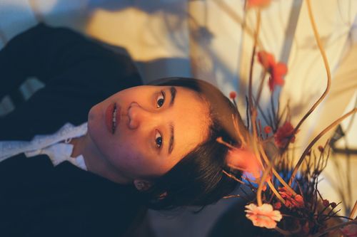 Free Artistic portrait of a woman lying down with pink flowers. Soft lighting creates a warm, serene ambiance. Stock Photo