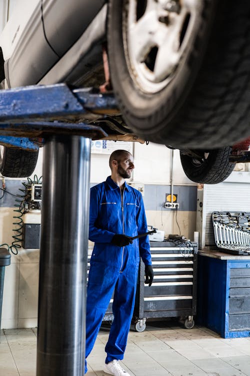 Free Man In Blue Coverall Standing Under A Vehicle With A Tool Stock Photo