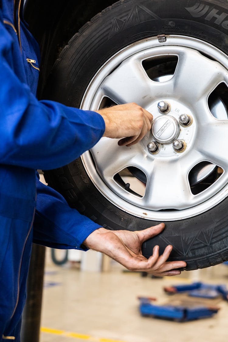 A Person In Blue Jumpsuit Holding The Car Tire