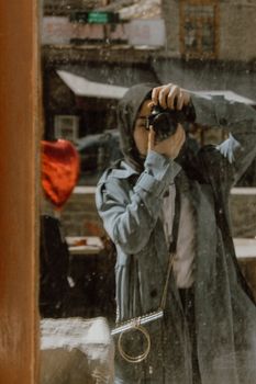 Reflection shot of a person taking a photo with a DSLR camera in urban setting.