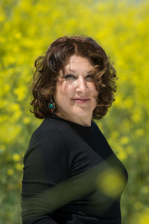 Free A mature woman smiling in a field of yellow flowers, capturing a serene moment outdoors. Stock Photo