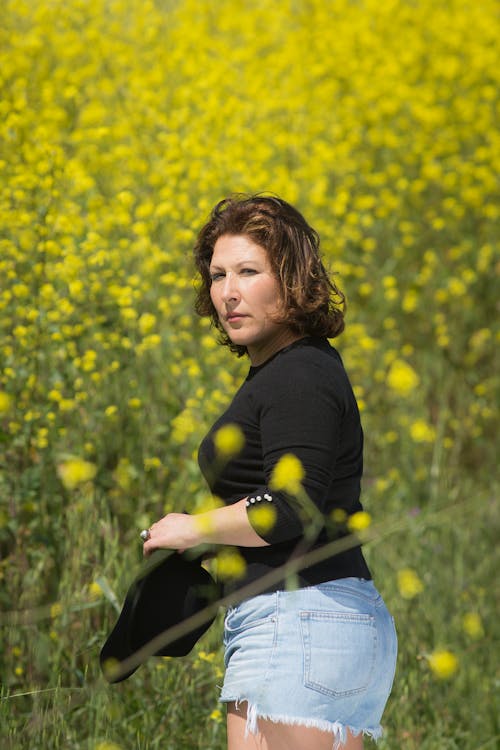 Free Woman in Black Long Sleeve and Blue Denim Shorts Standing on Yellow Flower Field Stock Photo