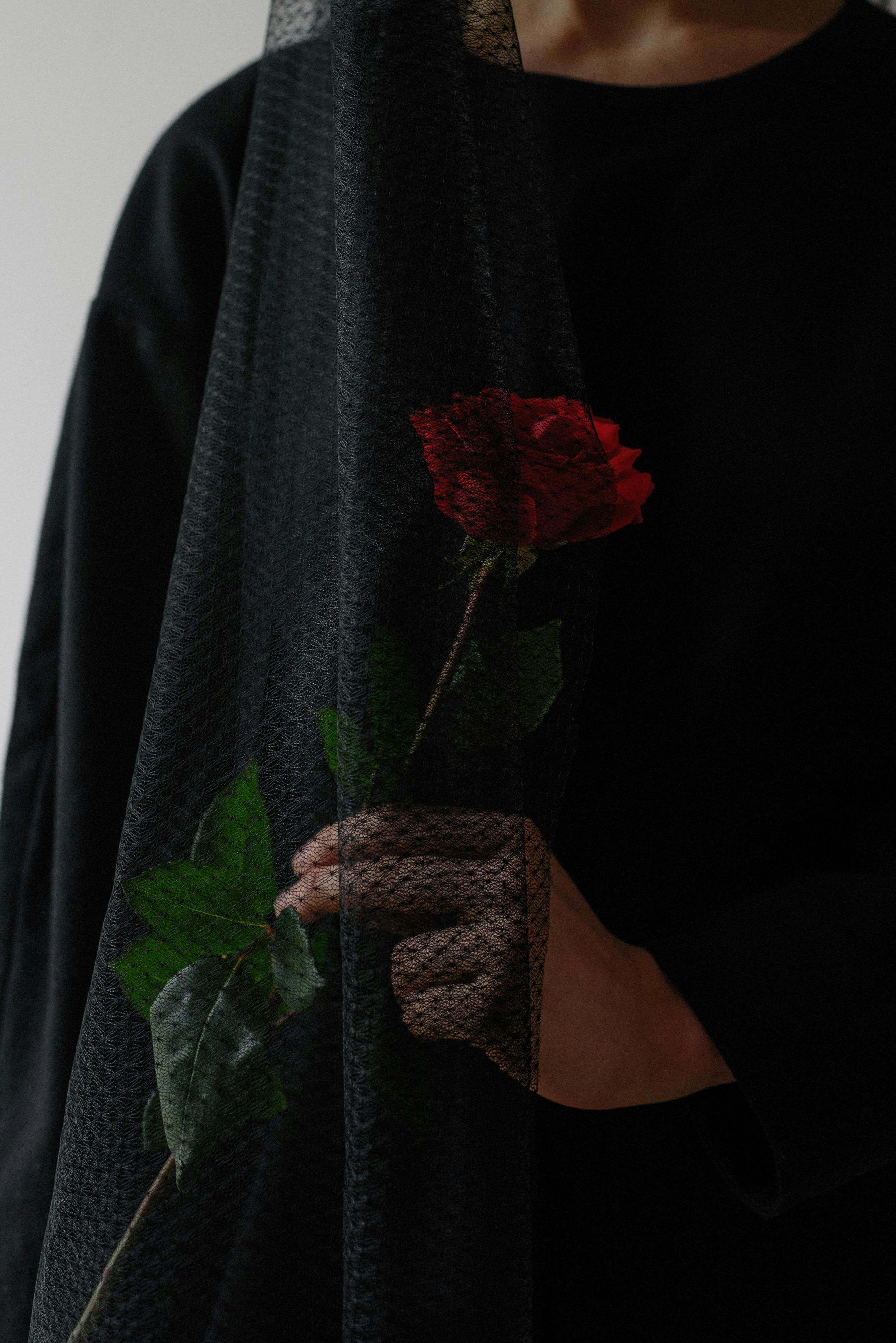 A person in black attire holding a red rose symbolizing grief during mourning.