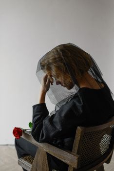 A woman wearing a black veil holds a red rose, symbolizing grief and reflection.