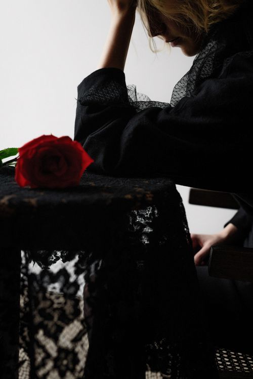 Free A woman in mourning attire with a red rose on lace against a stark background. Stock Photo