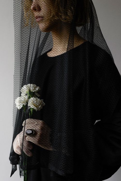 Free A woman wearing a black veil holds white flowers in a solemn, indoor setting. Stock Photo