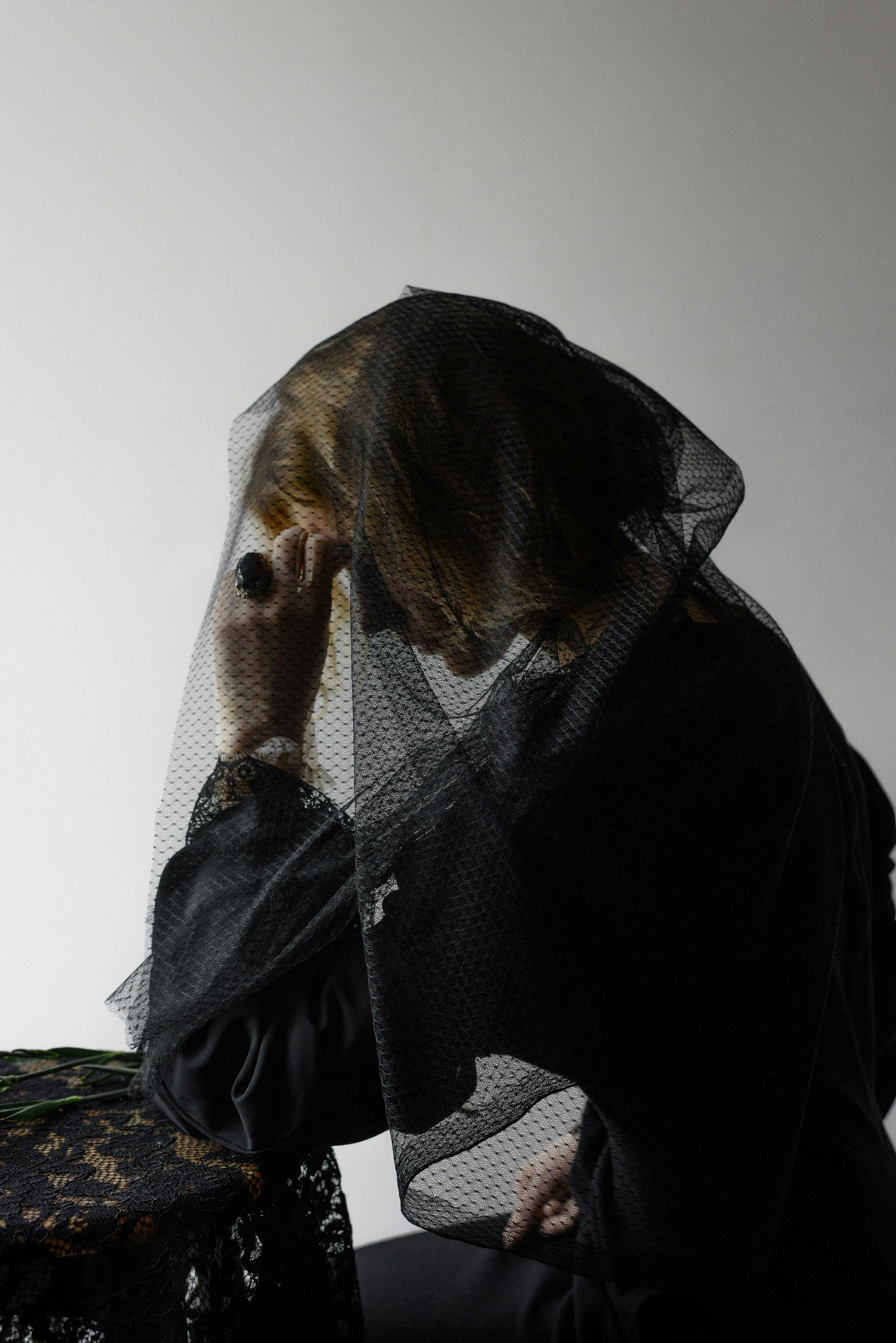 A woman in a black mourning veil sitting in reflection, capturing a somber and contemplative mood.