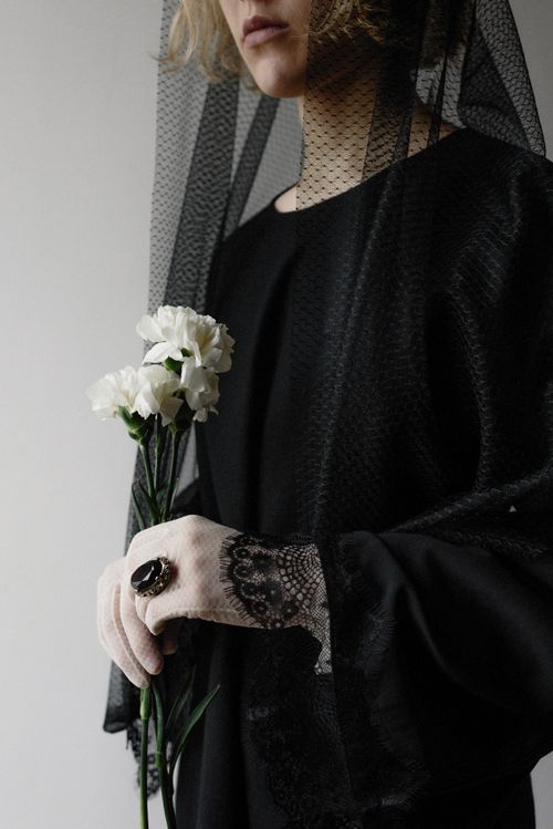 Free Portrait of a woman in black attire holding white carnations, featuring lace gloves and a large ring. Stock Photo