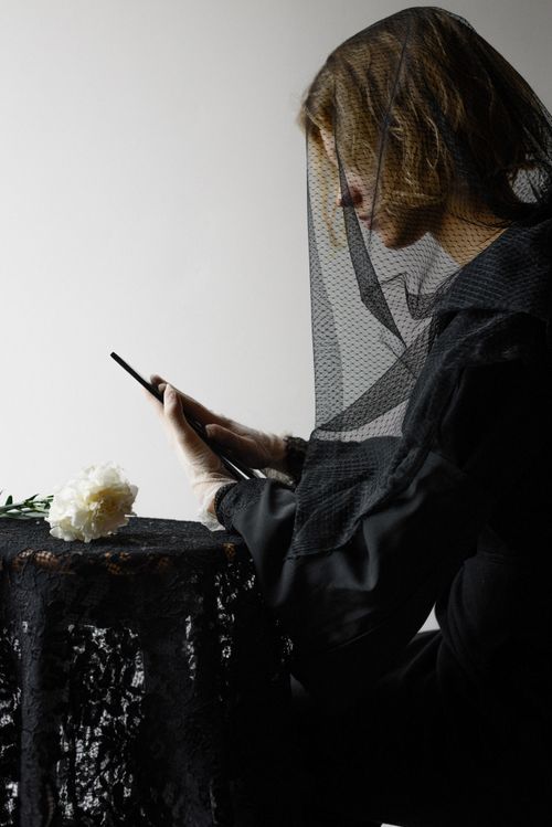 Free Woman in black dress and veil pensively holding a rose, embodying grief and elegance. Stock Photo
