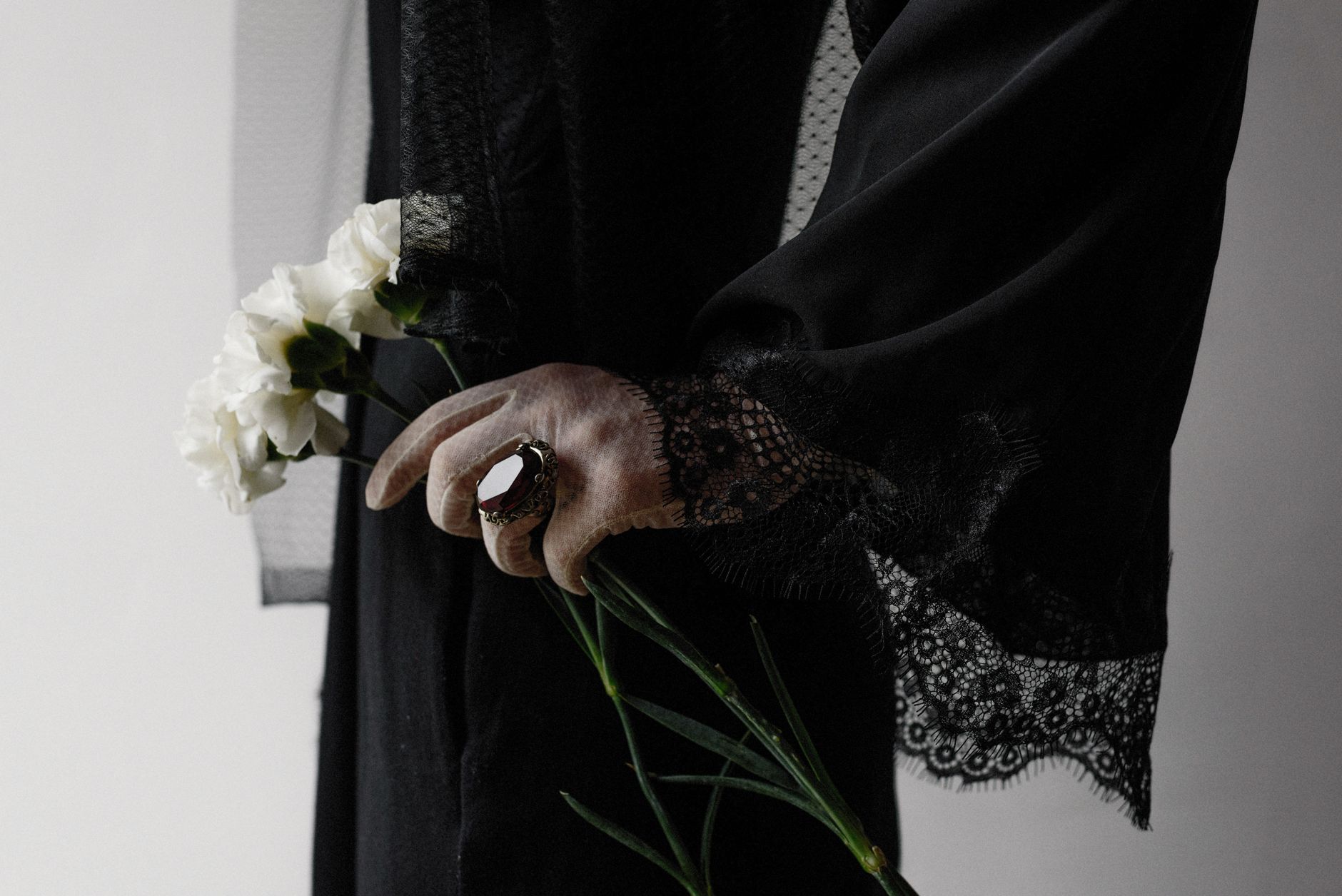 Close-up of a woman in black lace dress holding white flowers, symbolizing mourning and elegance.