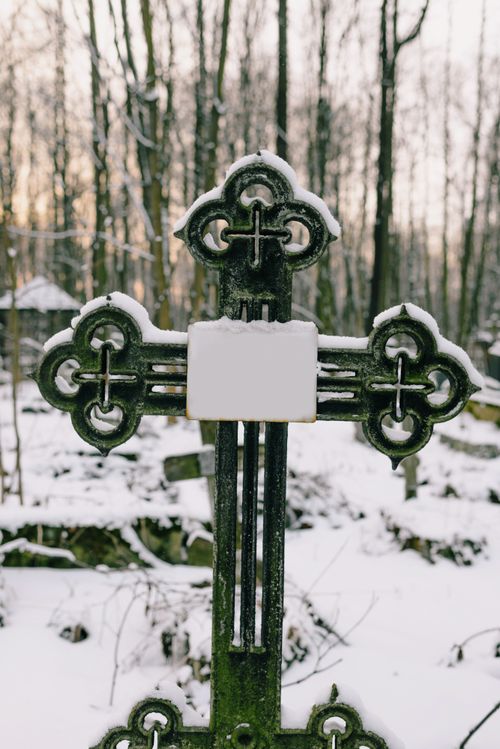 Free A snowy metal cross in a tranquil winter cemetery setting with bare trees. Stock Photo