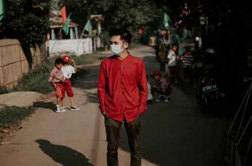 Free Young man in a red shirt wearing a face mask standing on a sunny street. Stock Photo