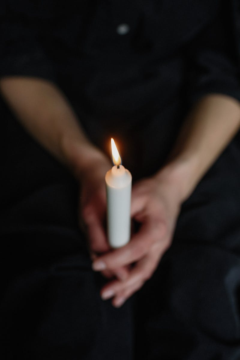 Close-up of hands holding a lit candle in a dark setting, symbolizing hope and serenity