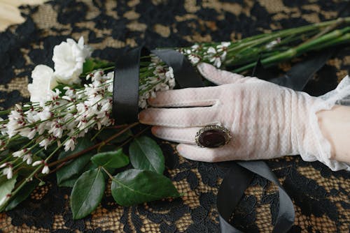 Person in White Lace Gloves Holding White Flowers