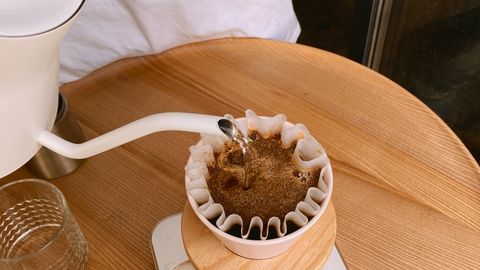 Close-up of hand pouring coffee using filter on wooden table. Ideal for coffee enthusiasts.