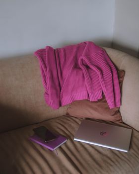 A pink sweater draped over a sofa with a laptop and notebook nearby, creating a cozy vibe.