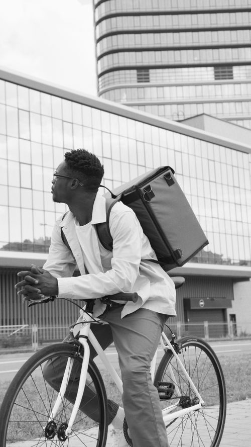 Free Black and white photo of a man with a bicycle and backpack in an urban setting. Stock Photo