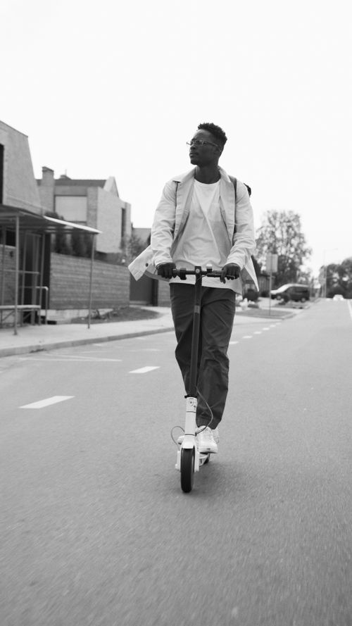 Free Black and white image of a man riding an electric scooter on an urban street. Stock Photo