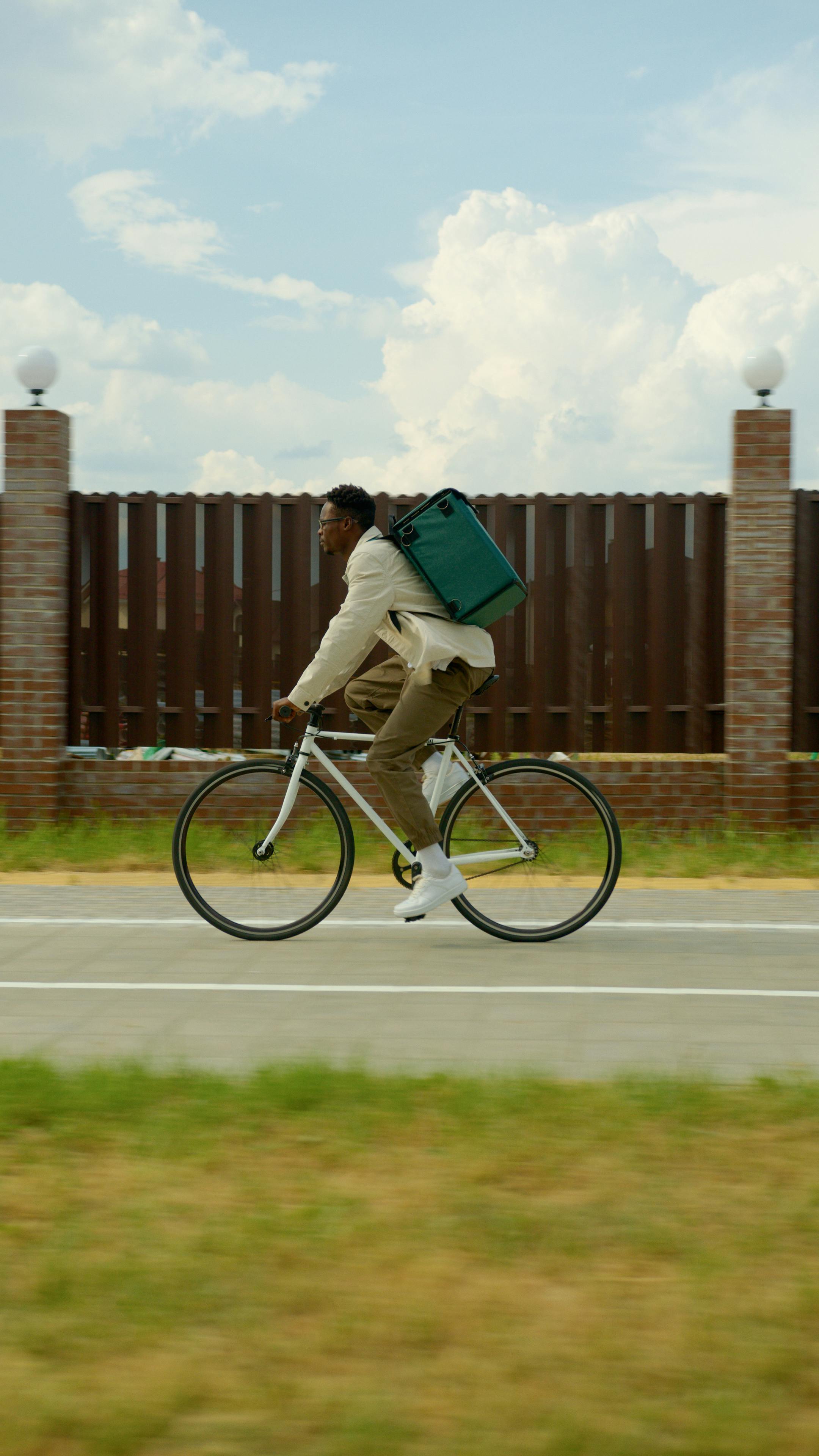 photo of a deliveryman riding a bicycle against a fence