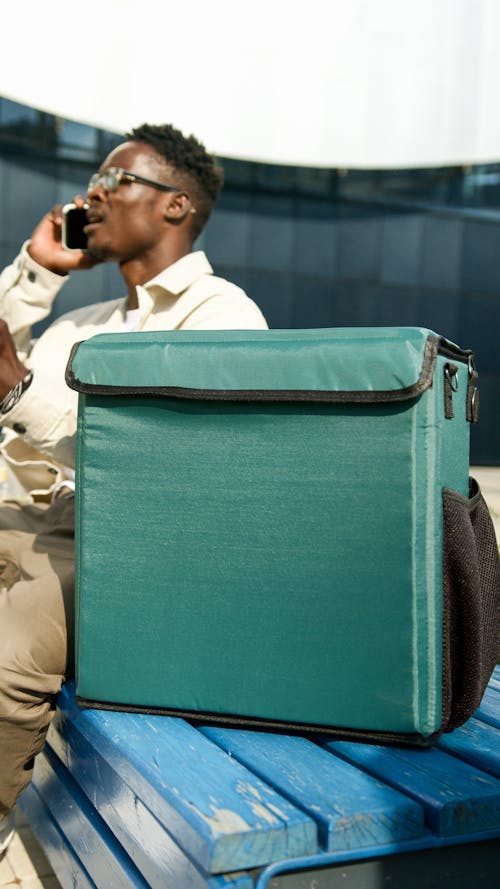 Photo of a Deliveryman Speaking on a Phone, and a Green Bag in the Foreground