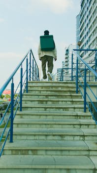 A food delivery person with a thermal bag climbs stairs in a modern urban environment, showcasing city life.