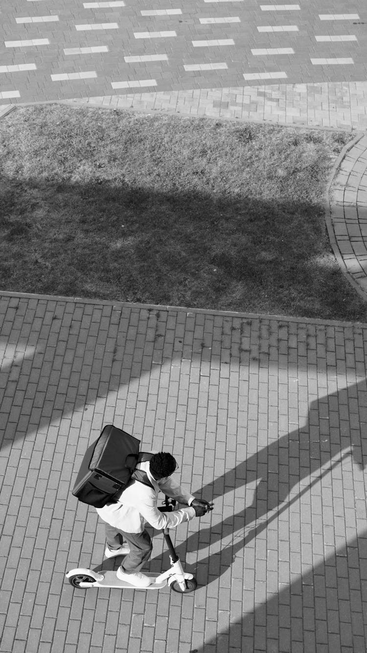 A Grayscale Of A Man Riding A Scooter