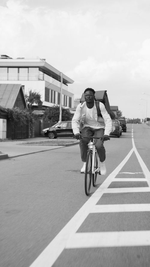 Free Black man biking on an urban road, portrayed in monochrome, adding a classic touch. Stock Photo