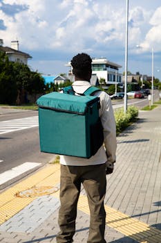 Back view of a delivery person carrying a thermal bag on a sunny street.