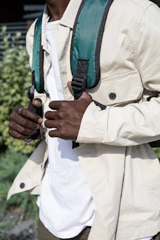 An adult man with a backpack, dressed in white long sleeves, walking outdoors. 