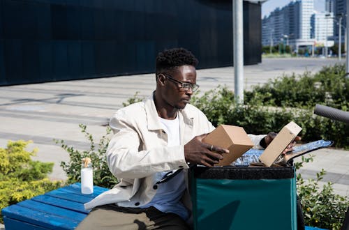 Man in White Dress Shirt Sitting on Blue Bench Looking at Parcels