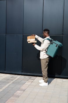 Side view of a delivery person holding packages against a modern urban backdrop.