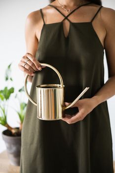 Stylish woman in green dress holding a sleek gold watering can indoors.
