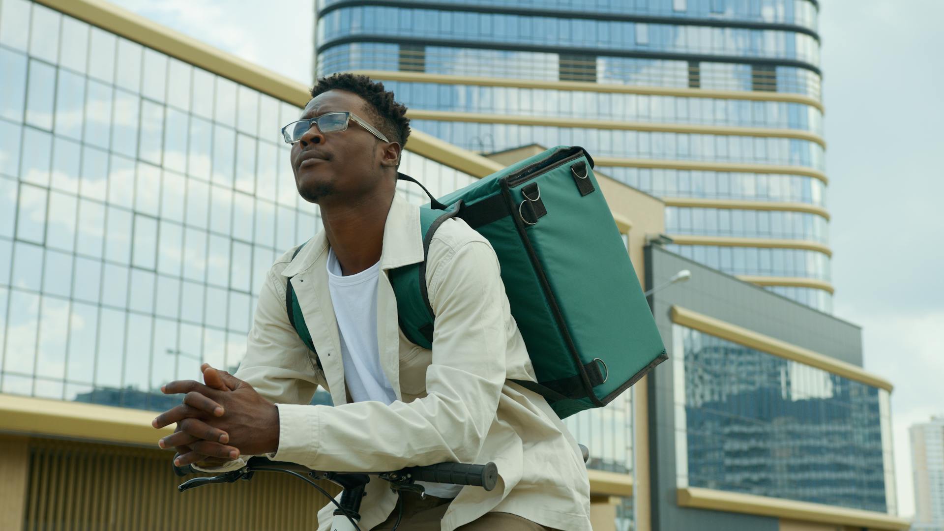 Delivery man biking through urban cityscape with modern architecture, ready for fast and eco-friendly delivery service.
