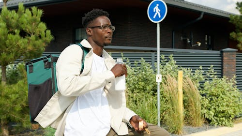 A Man with a Backpack Standing Near a Street Sign Drinking Milk