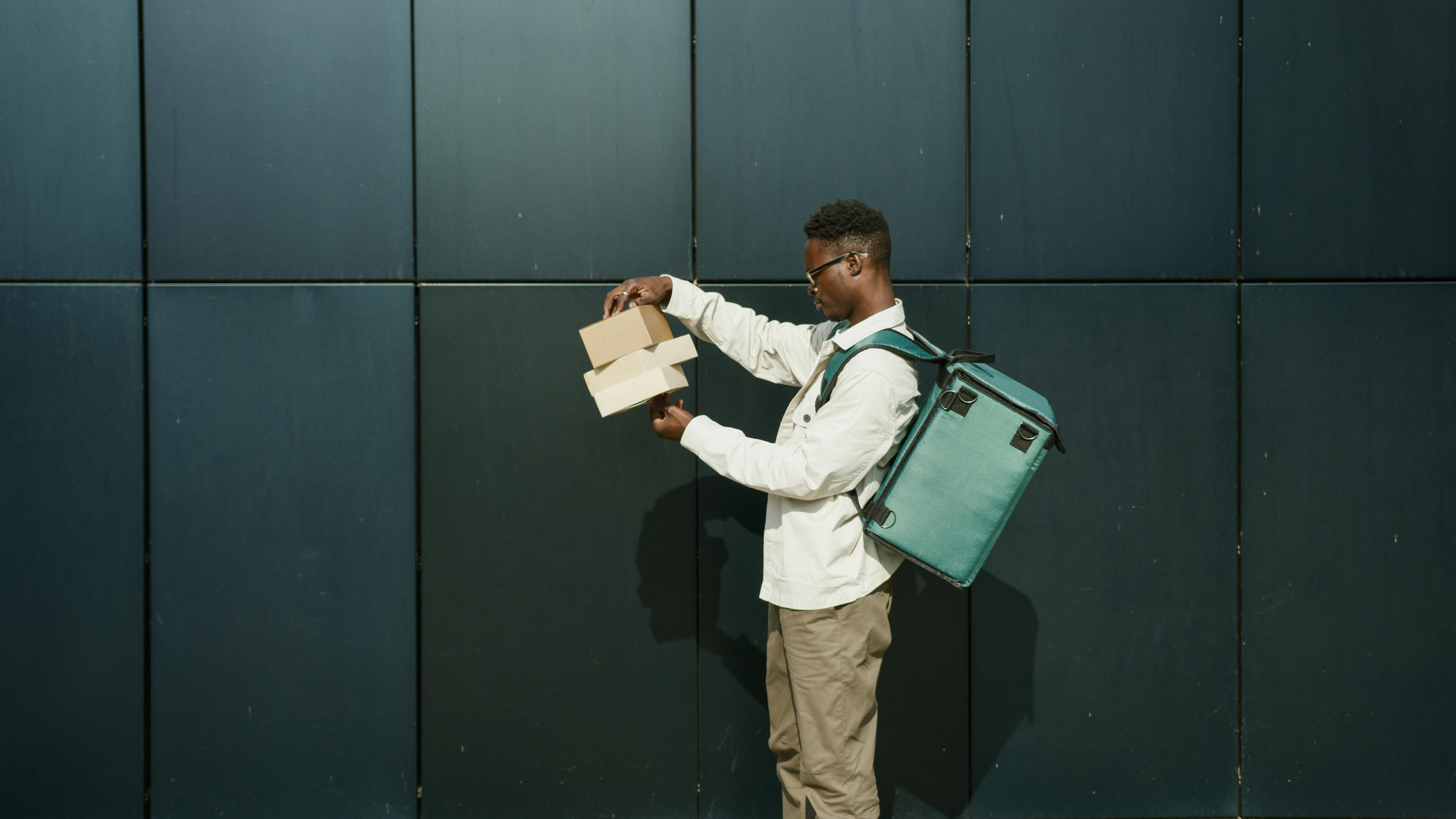 A man with a backpack and laptop stands before a wall, representing Tim Hortons Foundation Camps' commitment to youth empowerment.
