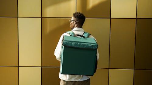 Man Carrying a Delivery Bag Standing Beside a Brown Wall