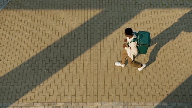 High angle view of a person walking on a paved pathway with a backpack outdoors.